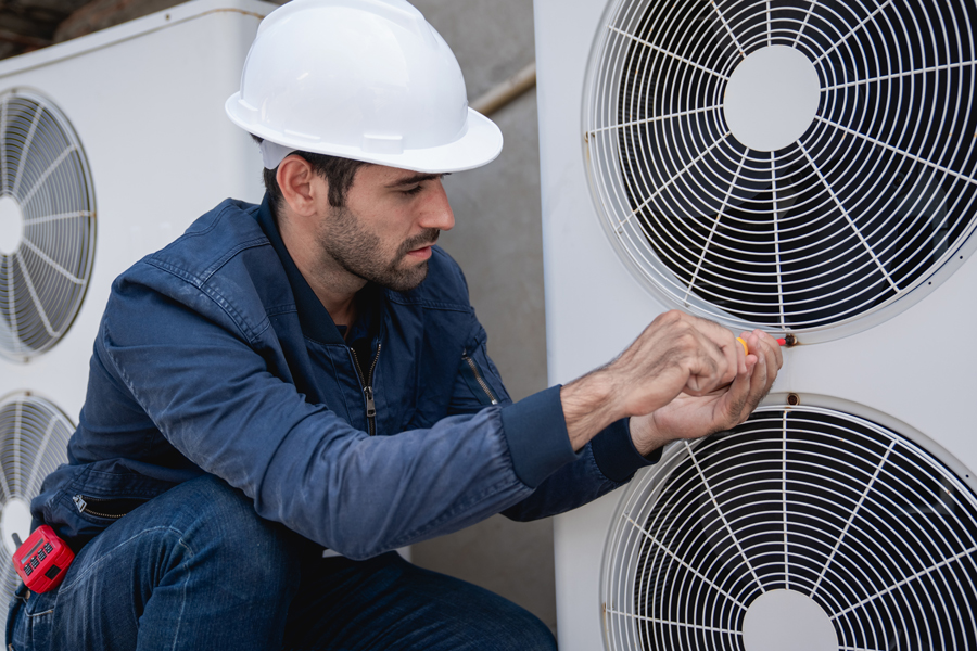 Technician in hard hat and blue shirt working on a heat pump