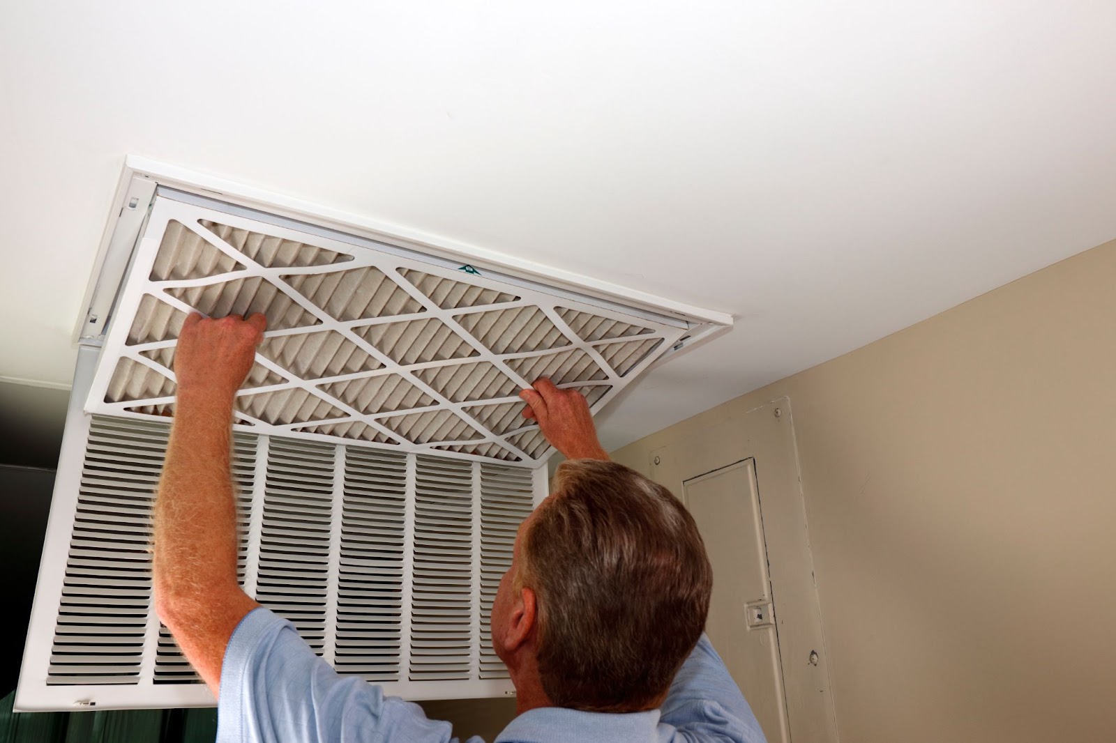 A man installs an air filter in the ceiling as part of winterizing the HVAC system and ductwork replacement.