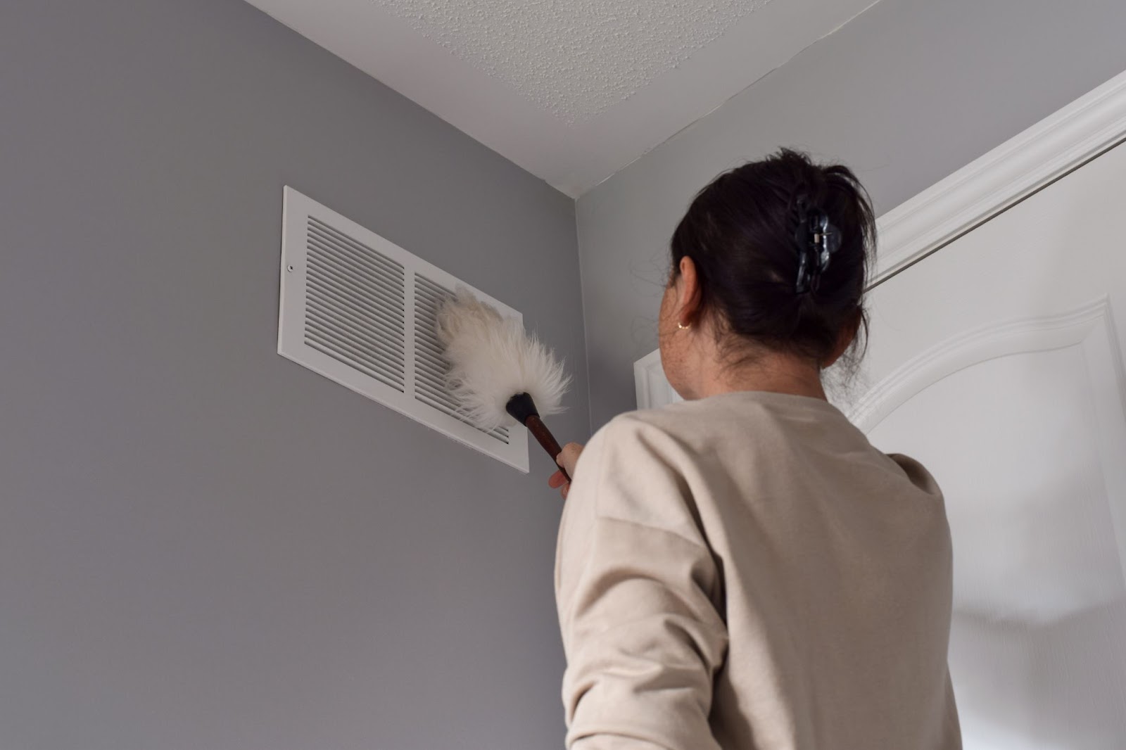 A woman using a brush to clean a vent, ensuring proper maintenance of her HVAC system for winter readiness.