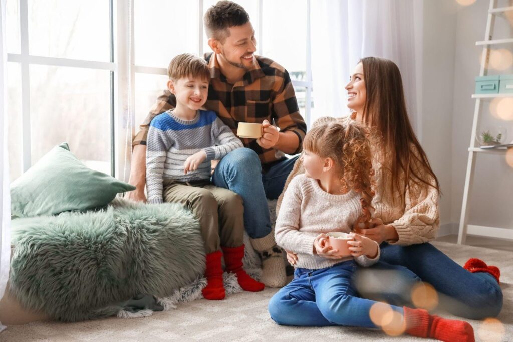 A family sits on the floor, sharing moments of joy and connection in front of a bright window