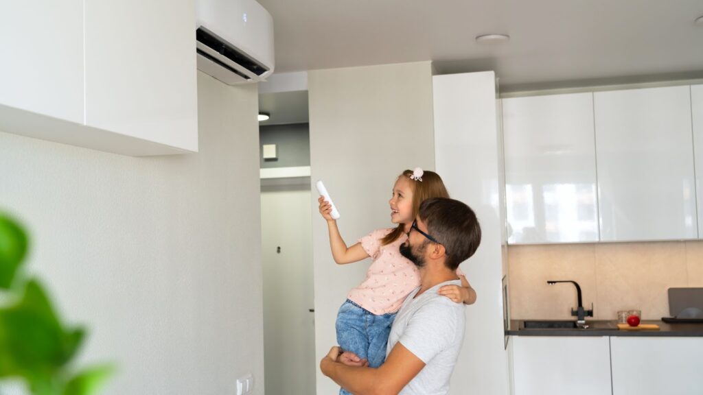 A man and a young girl stand beside a wall-mounted air conditioner, highlighting the importance of air duct sealing services.